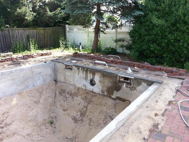 253: The first few concrete blocks go down at the deep end of the pool.  We cut four 2-foot lintels out of 1/8 aluminum stock to help support the block above the skimmer.